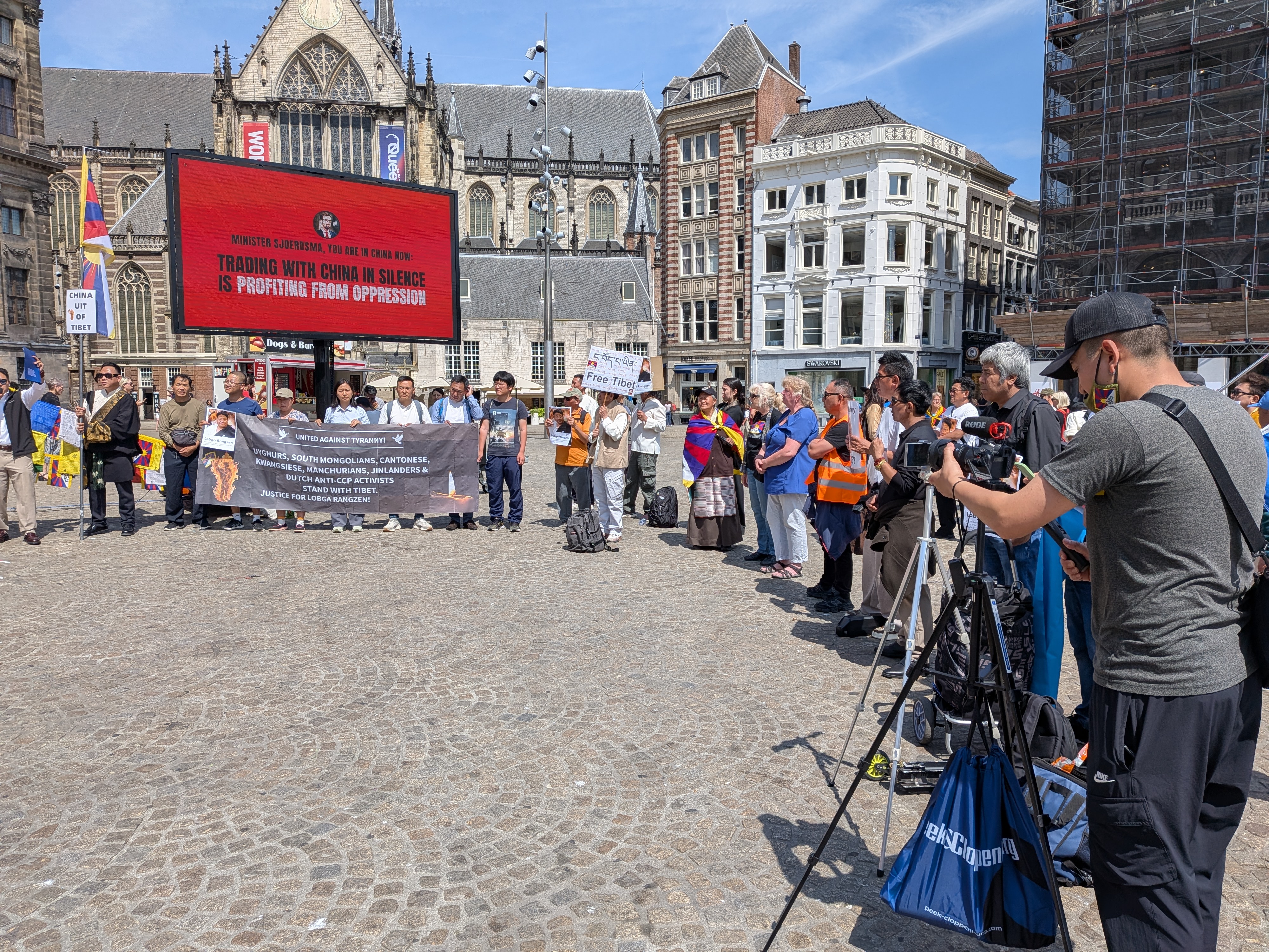 Groot videoscherm op de Dam met de boodschap: Minister Sjoerdsma, you are in China now — Trading with China in silence is profiting from oppression, naast een solidariteitsspandoek