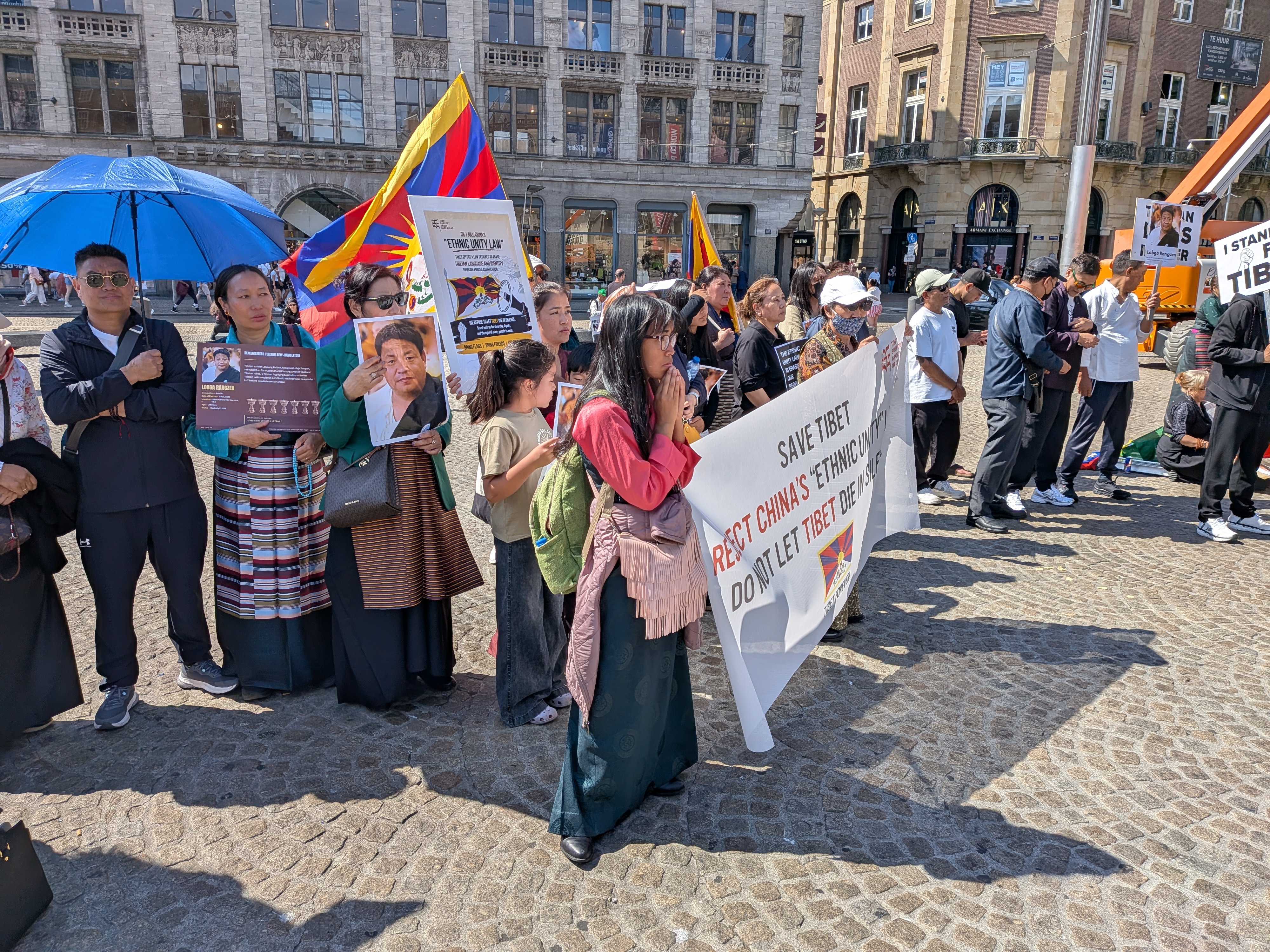 Tibetanen in traditionele kleding bidden bij de gedenkplaats, met portretten van Lobga Rangzen en het spandoek Save Tibet — Reject China's Ethnic Unity Law