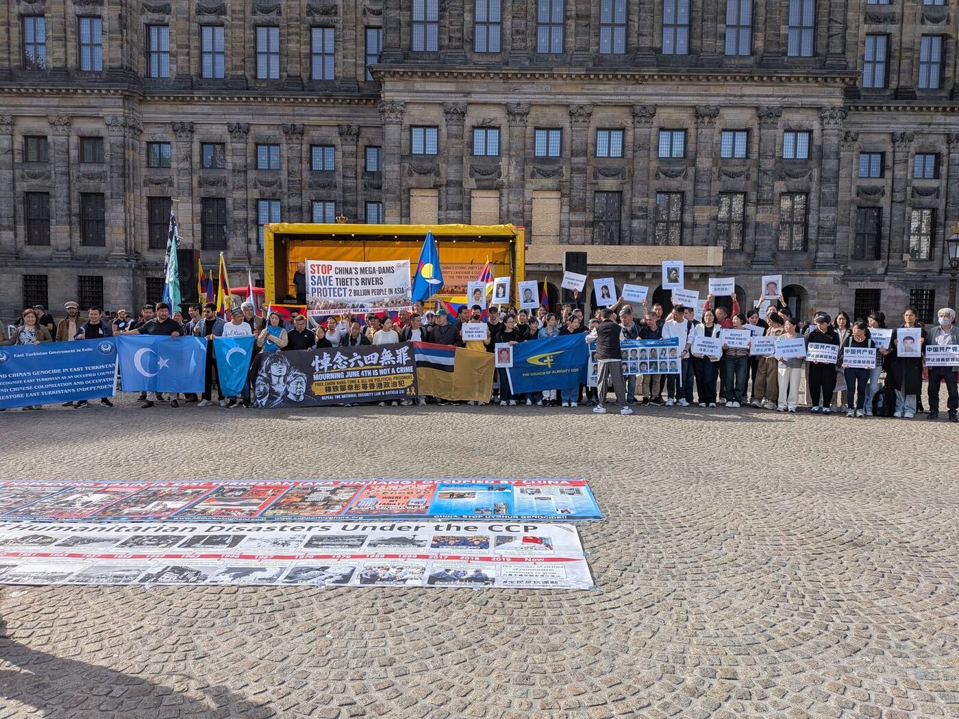 Deelnemers met vlaggen en spandoeken van Oost-Turkestan, Zuid-Mongolië, Hongkong en Tibet voor het Koninklijk Paleis op de Dam