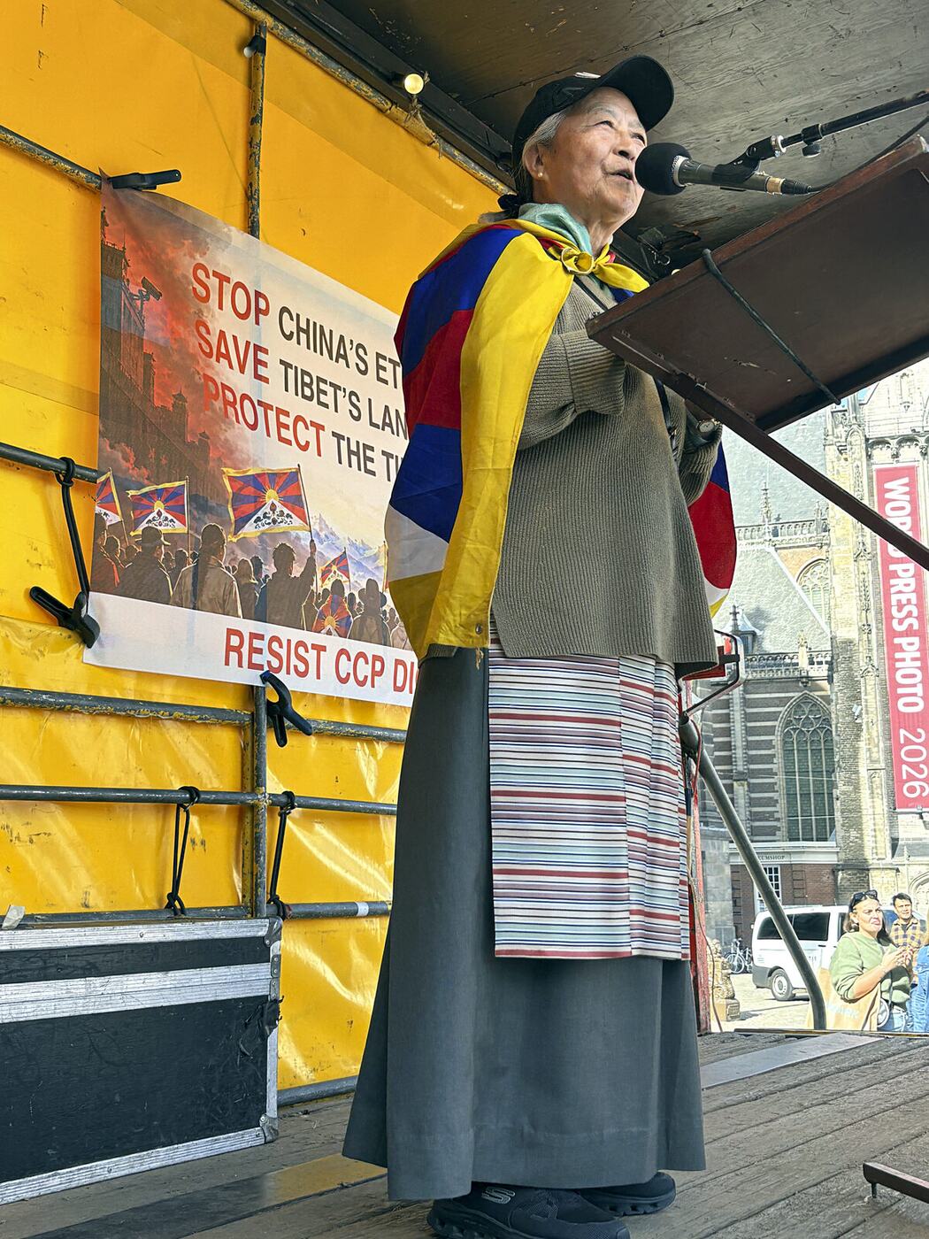 Tibetaanse spreekster met de Tibetaanse vlag om haar schouders achter de microfoon op het podium op de Dam